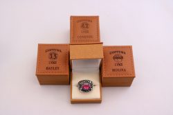 Four Chippewa Lynx ring boxes arranged with a ring in the center box. Boxes are labeled Hayley, Coveyou, and Molina. The ring has a pink stone. 